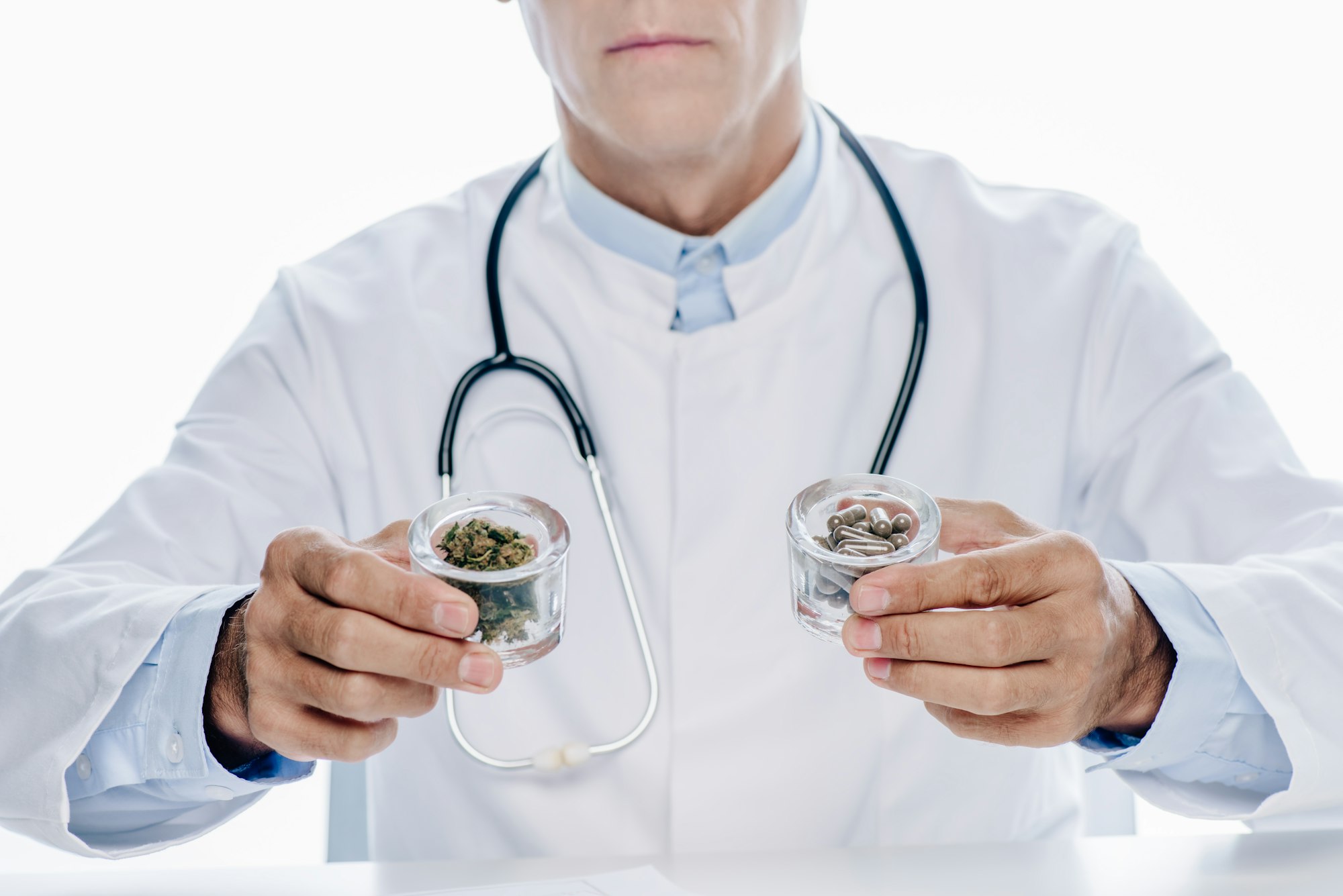 cropped view of doctor in white coat holding pills and medical cannabis isolated on white